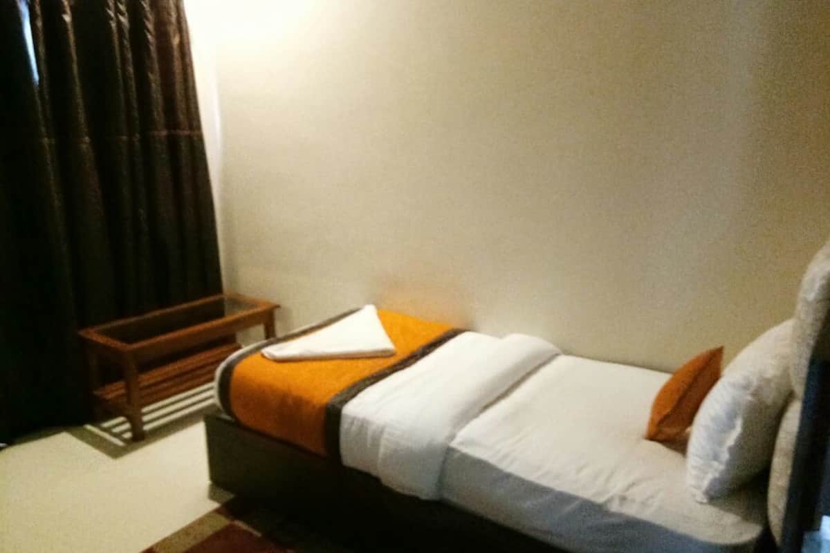 A single bed with a white and orange bedspread, a wooden nightstand, and a dark curtain.
