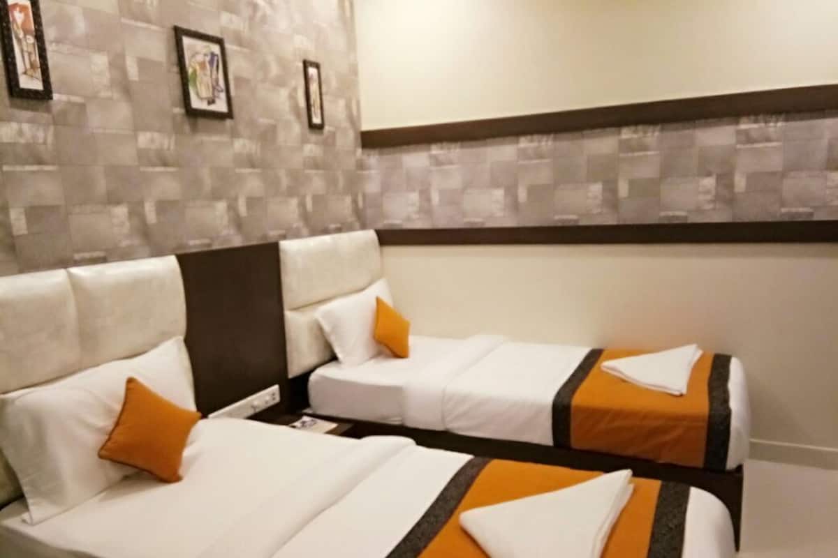 A hotel room with two beds, each with white bedding and orange accents. The room has a tiled wall with framed pictures and a brown trim at the top.