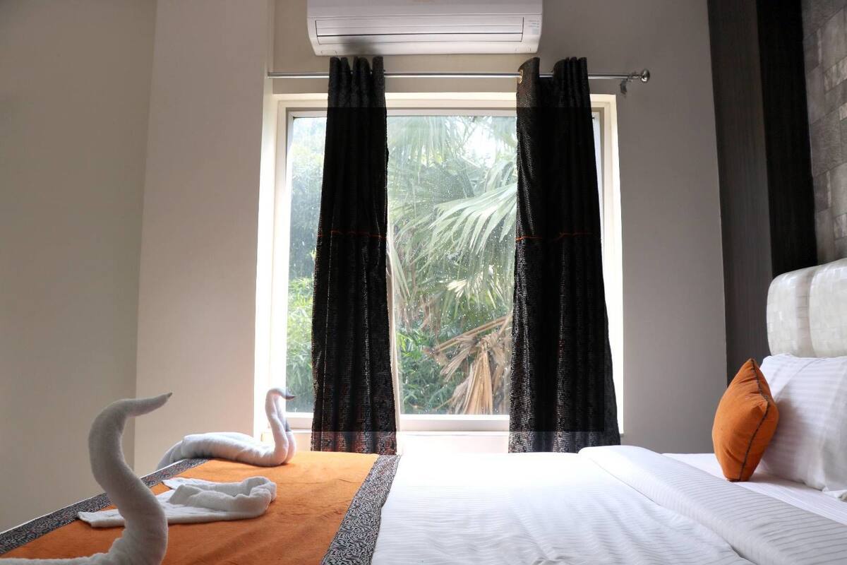 A hotel room with a bed, a window with curtains, a swan decoration, and a towel on the bed.