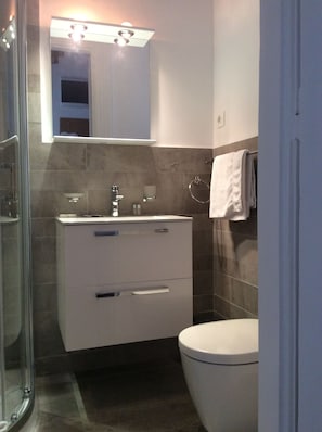 Un baño moderno con cabina de ducha de vidrio, un tocador blanco con espejo y un inodoro.