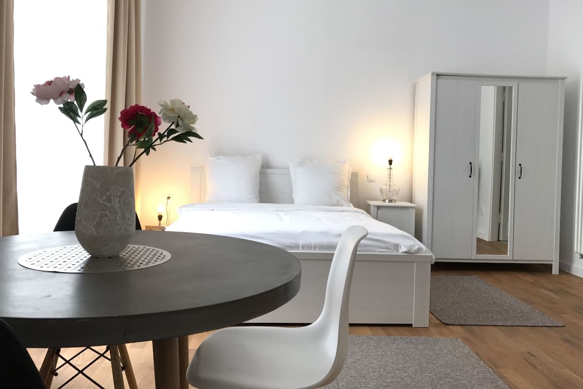 A modern bedroom with a bed, bedside table, lamp, wardrobe, and a dining table with chairs.