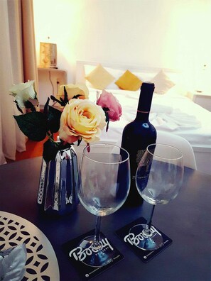 Una mesa con un jarrón de flores, dos copas de vino y una botella.