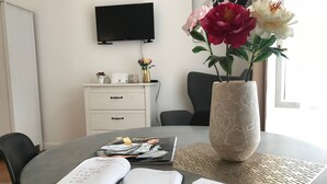 Ett arbetsområde med ett runt bord, en bok, en penna, en vas med blommor, en tv och ett vitt skåp.