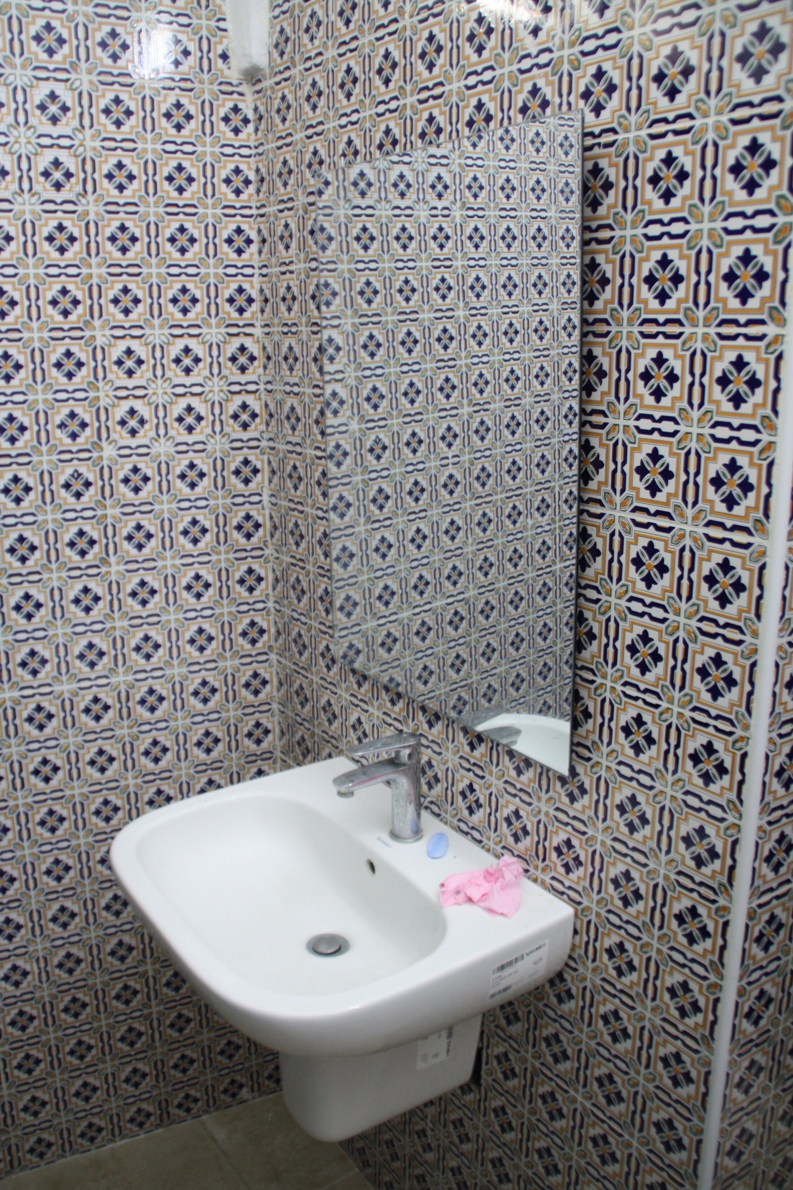A bathroom with patterned tiles, a white sink, and a mirror.