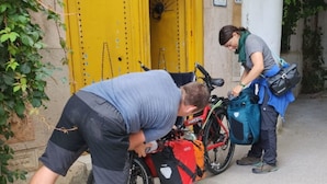 Two people handling a bicycle and a red bag near a yellow door. - Hostel El Medina (Tunis)