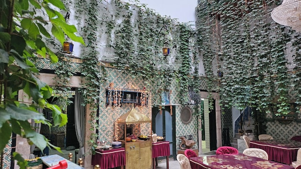 An outdoor dining area with tables and chairs, surrounded by ivy-covered walls and traditional decor. - Hostel El Medina (Tunis)