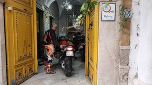 A yellow door with a sign above it, a motorcycle parked inside, and a person standing next to it. - Hostel El Medina (Tunis)