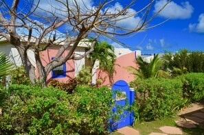 A building with a pink and white exterior, a blue gate, and a tree in the foreground. - Villas at Indigo Reef (West End Village)