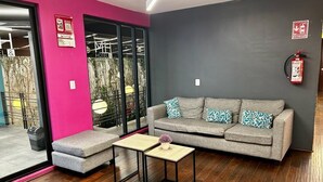 A modern hotel lobby with a grey sofa, a small table, and a pink accent wall. - Hotel MH (Chignahuapan)