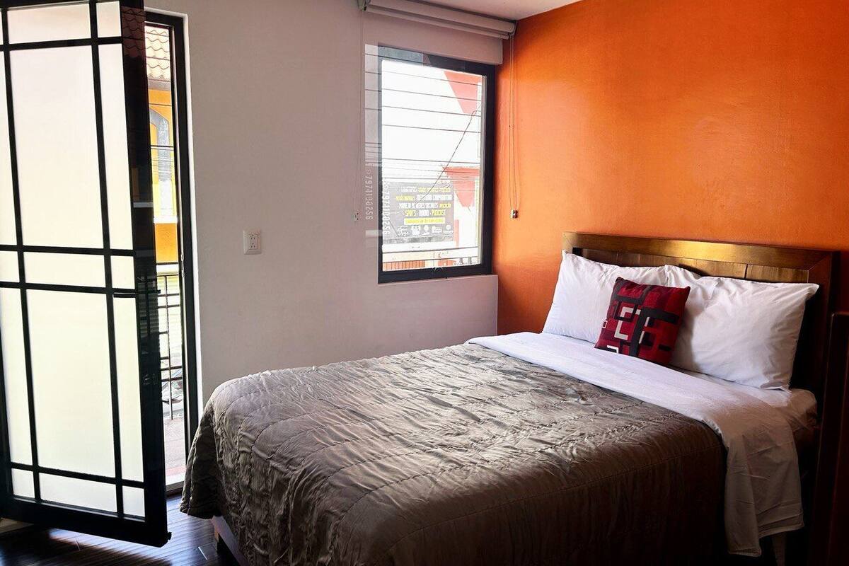 Un dormitorio con cama, ventana y pared naranja.