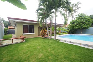 A house with a swimming pool, a lawn, and palm trees. - Jaco Villa 42 (León XIII)