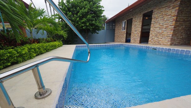 A swimming pool with a tiled edge, a metal handrail, and a stone building in the background. - Jaco Villa 42 (León XIII)
