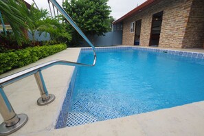 A swimming pool with a tiled edge, a metal handrail, and a stone building in the background. - Jaco Villa 42 (León XIII)