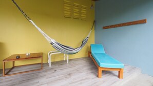 A room with a hammock, a blue sofa, a wooden table, and a wall-mounted shelf. - Jaco Villa 42 (León XIII)