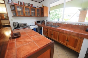 A kitchen with wooden cabinets, a tiled countertop, a stove, a microwave, and a sink. - Jaco Villa 42 (León XIII)