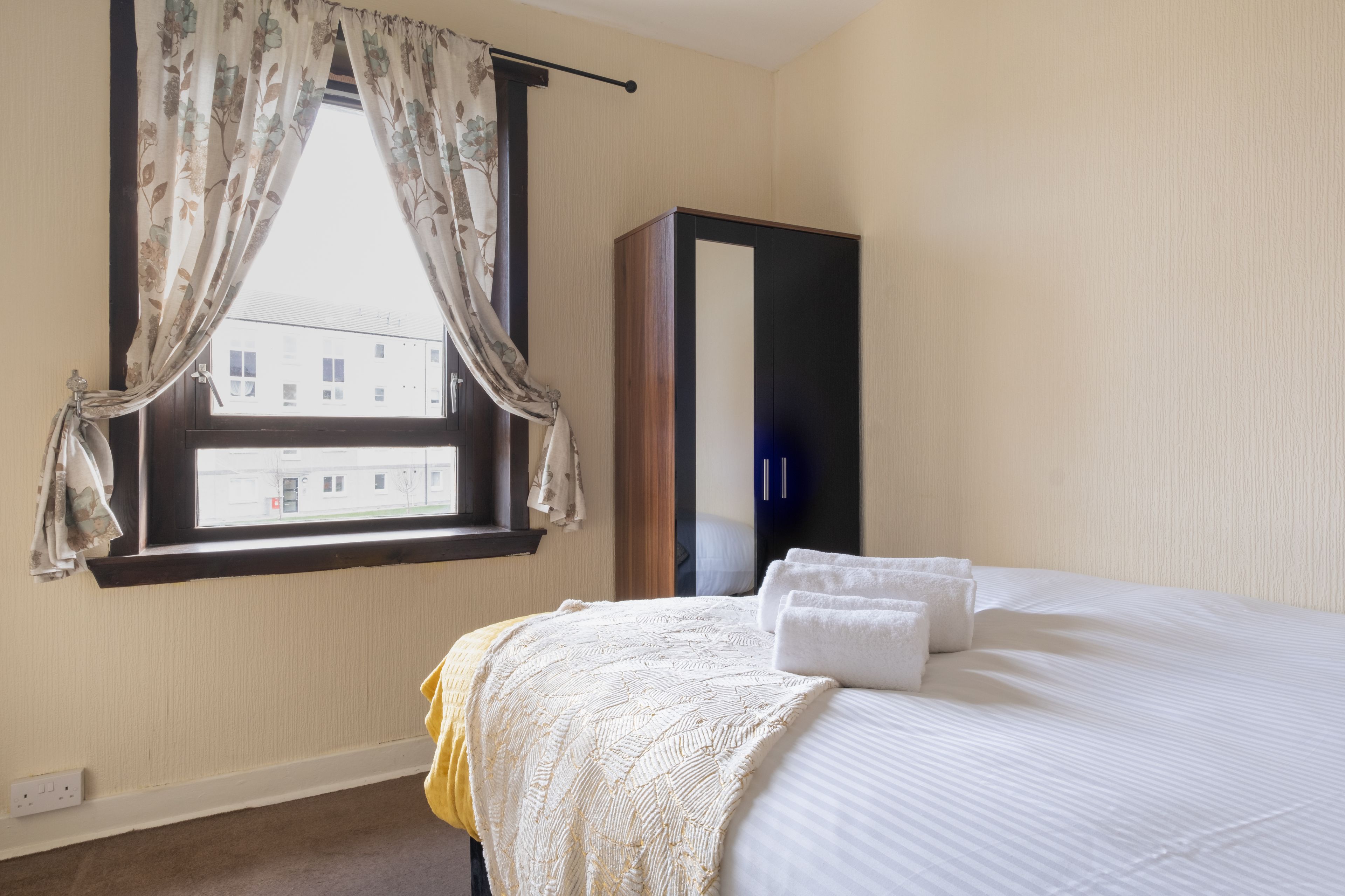 Een hotelkamer met een bed, een kledingkast en een raam met gordijnen.