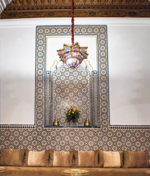 A room with intricate tile patterns, a hanging chandelier, and a sofa with cushions.
