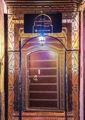 A hotel entrance with a decorative iron gate, a sign above the door, and a doormat at the bottom.