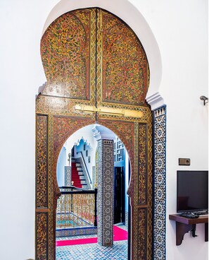 An ornate doorway with intricate patterns, leading to a room with a tiled floor and a red carpet.
