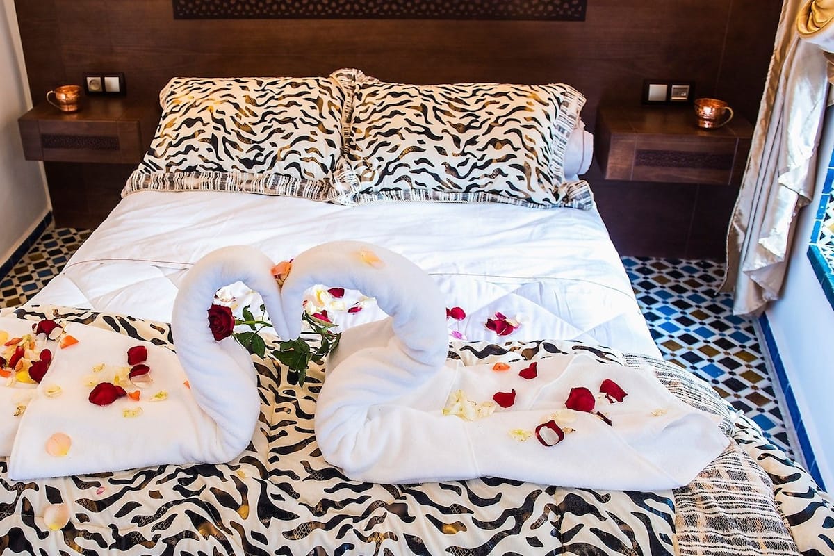 A bed with a zebra print bedspread, two swan-shaped pillows, and scattered rose petals.