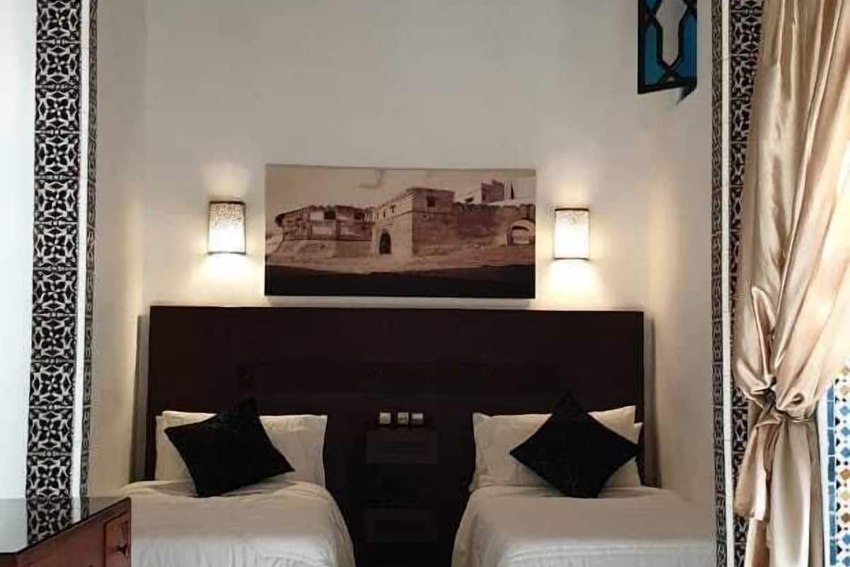 A room with two beds, a wooden headboard, patterned floor tiles, and a framed picture above the beds.