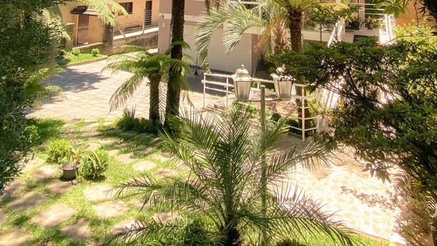 A two-story house with a sloped roof, surrounded by lush greenery and palm trees. - Pousada Vovô Nino (Gramado)