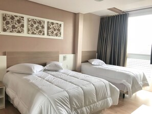 Ett hotellrum med två sängar, en sänggavel, ett nattduksbord och ett fönster med gardiner.