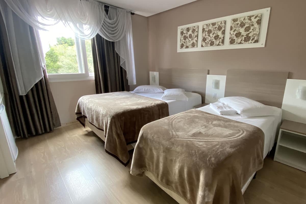 Habitación de hotel con dos camas, una ventana con cortinas y una pared con tres cuadros florales.