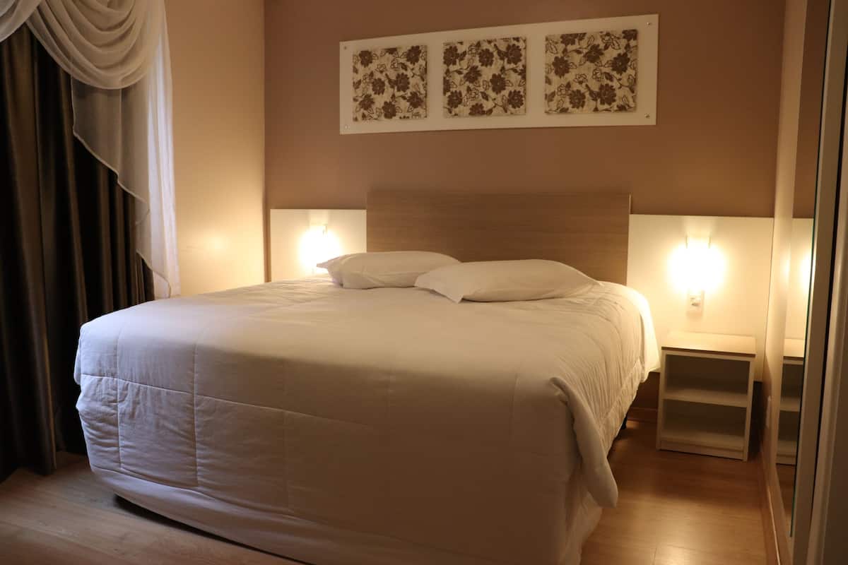 Una cama bien hecha con cabecera de madera, dos mesitas de noche con lámparas y decoración floral en la pared sobre la cama.