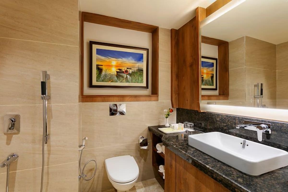 A modern bathroom with a large sink, a toilet, and a shower. There are framed pictures on the wall and a mirror above the sink.