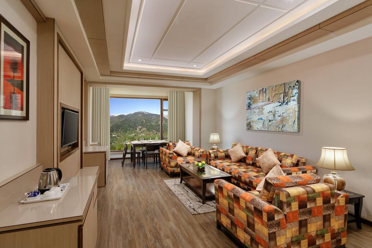 A modern hotel room with a sofa set, a TV, a dining area, and a painting on the wall.