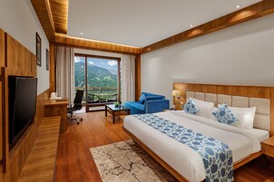 Camera d'albergo moderna con un letto grande, una TV, un balcone con vista sulle montagne e pavimento in legno.