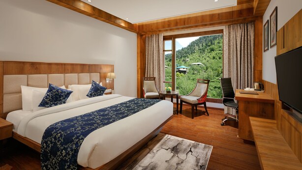 A modern hotel room with a large bed, a desk, a chair, and a TV. - The Orchid Manali - a Boutique Hotel (Manali)