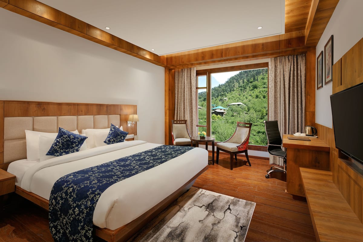 A modern hotel room with a large bed, a desk, a chair, and a TV.