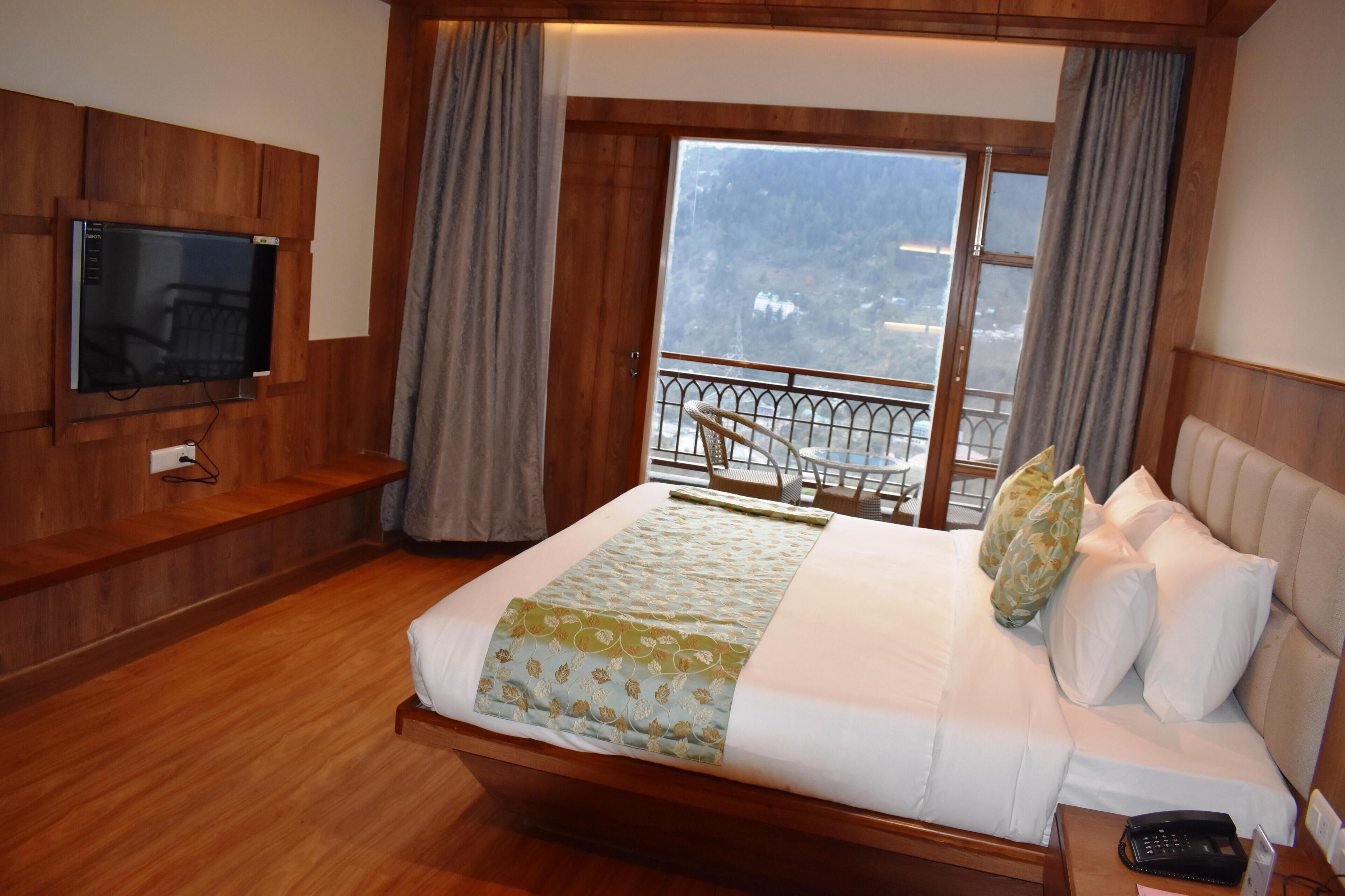Une chambre d’hôtel avec un grand lit, un téléviseur fixé au mur, un balcon avec une balustrade et une vue sur l’extérieur.