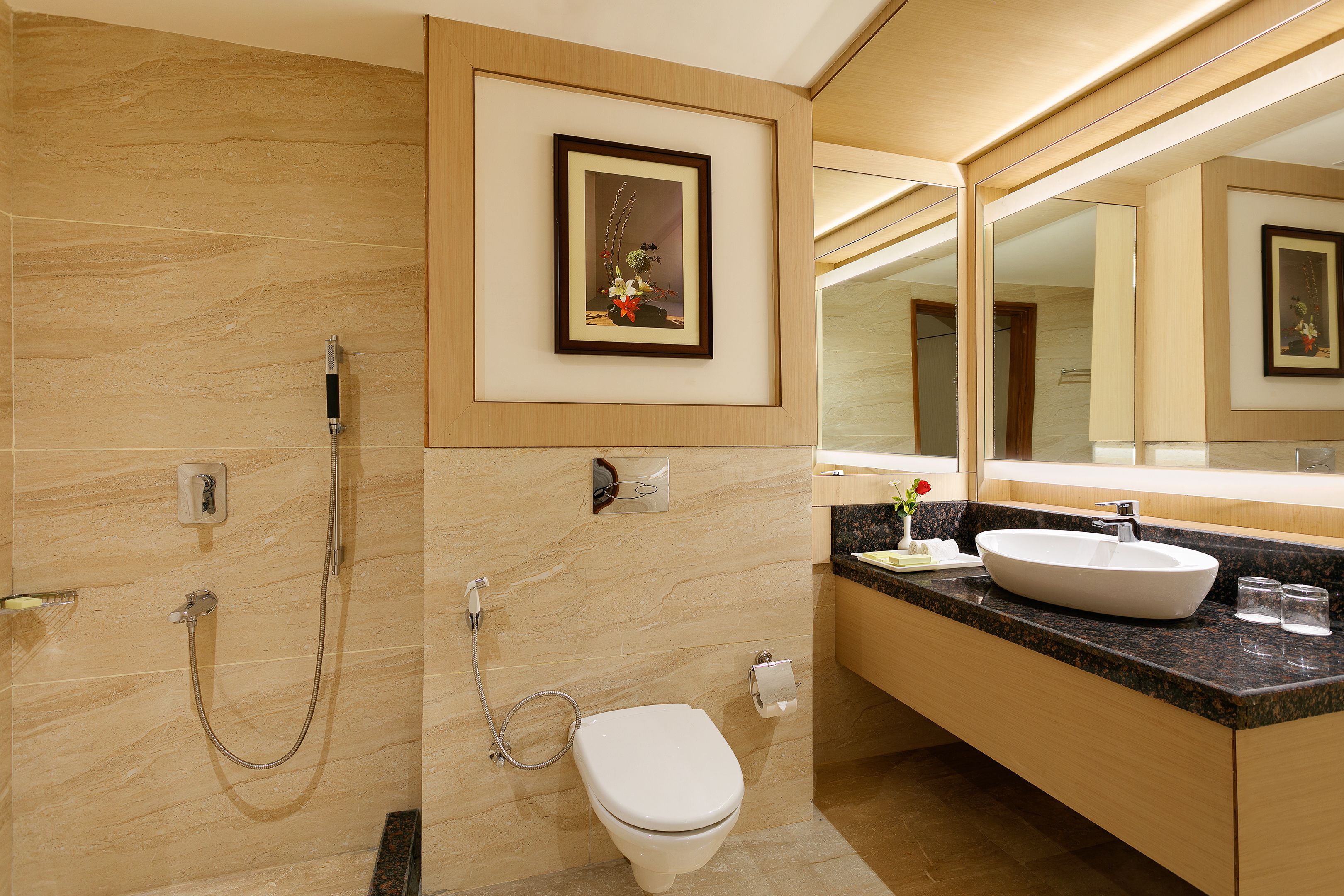 A modern bathroom with a marble floor, a white toilet, a sink with a large mirror above it, and a shower with a handheld showerhead.