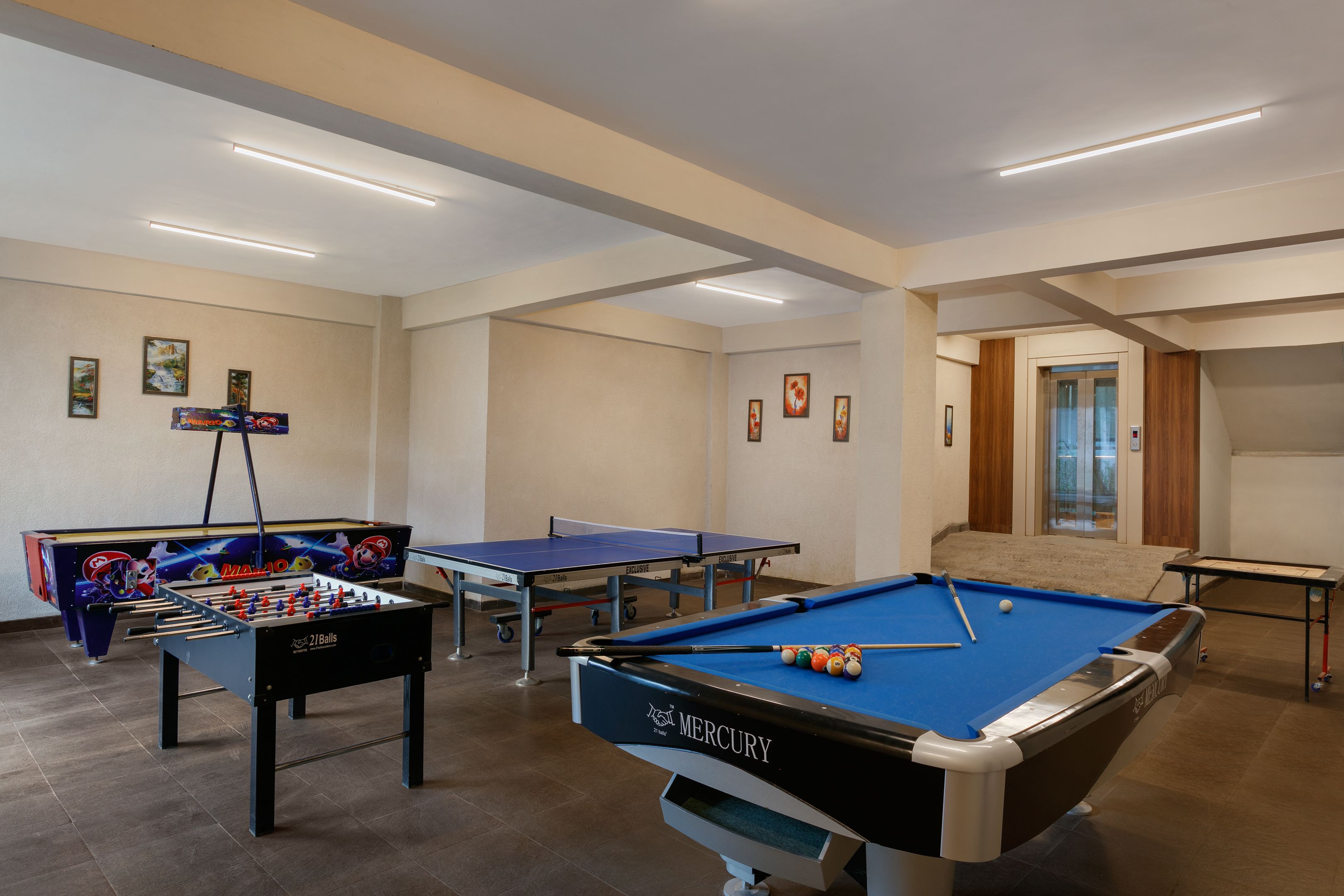 A pool table, foosball table, and ping pong table in a room with a tiled floor and a door in the background.