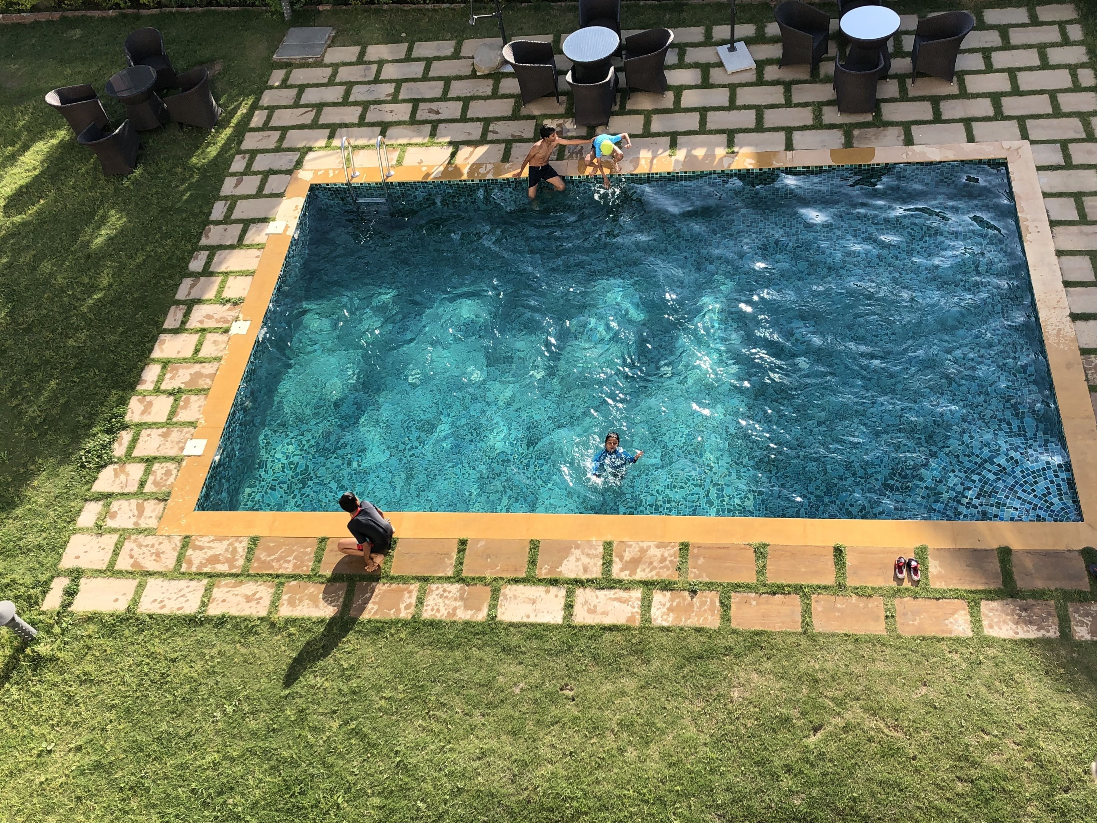 A rectangular outdoor swimming pool with a tiled edge, surrounded by a brick border and grass.
