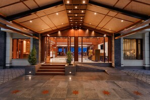A spacious lobby with a high ceiling, a central staircase, and a view of the interior through glass doors. - The Orchid Manali - a Boutique Hotel (Manali)