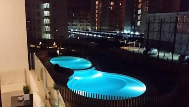 Une piscine sur le toit, dont les bords sont illuminés de lumière bleue, entourée de gratte-ciel la nuit.