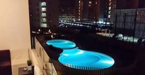 Une piscine sur le toit, dont les bords sont illuminés de lumière bleue, entourée de gratte-ciel la nuit.