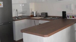 Une cuisine avec des meubles blancs, un réfrigérateur en acier inoxydable, un plan de travail en bois, un grille-pain et une machine à café.