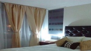 Une chambre d’hôtel avec un lit, des rideaux, une fenêtre et une tête de lit sombre.