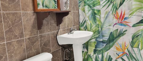 Baño con inodoro, lavabo y cortina de ducha con estampado de hojas tropicales.