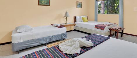A hotel room with two single beds, a large bed, a small table with a lamp, and a window with curtains.