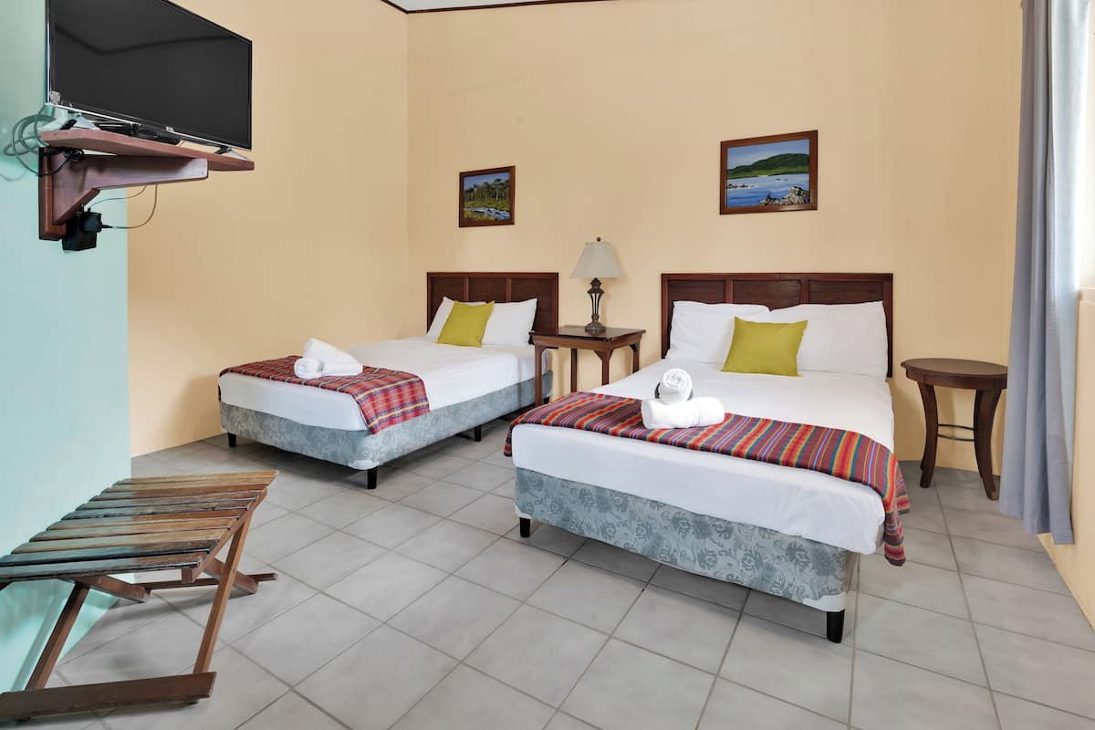 Habitación de hotel con dos camas, un televisor montado en la pared, una mesita con lámpara y una ventana con cortinas.