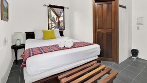 Una cama bien hecha con un edredón colorido, una lámpara de noche y una ventana con cortinas.