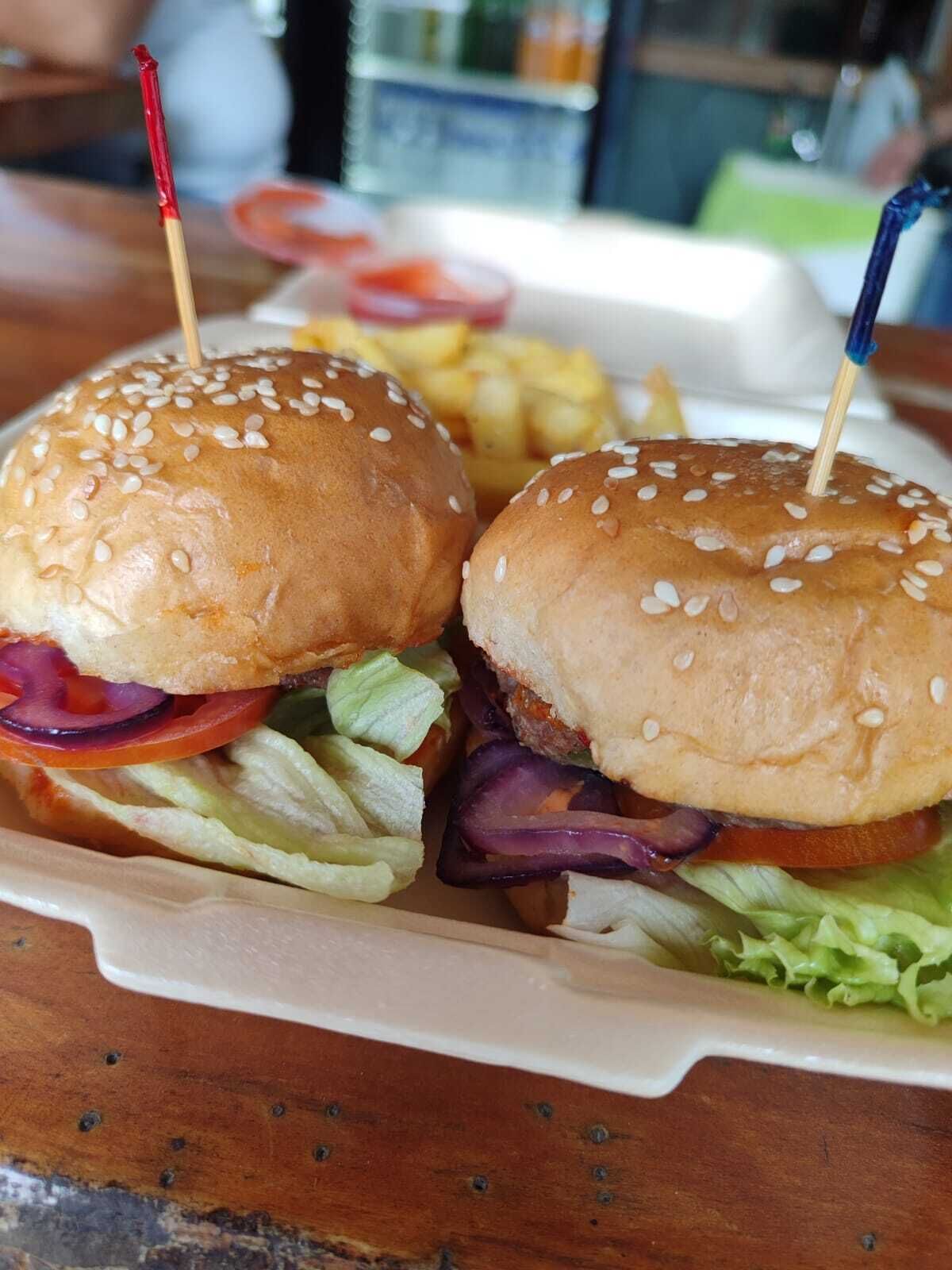 A sandwich with sesame seed buns, lettuce, tomato, and red onion, with a toothpick in each bun.