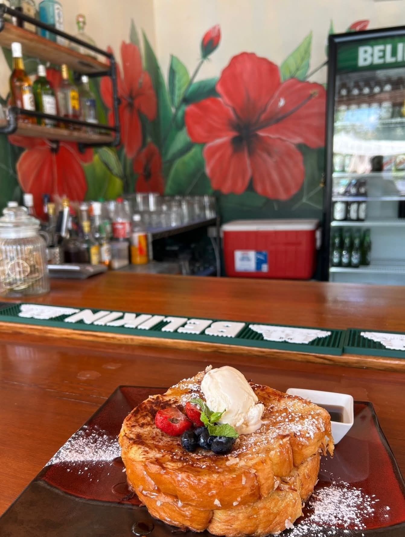 Een dessert met fruit en ijs op een bord, een bar met flessenkasten en een koelkast met drankjes.