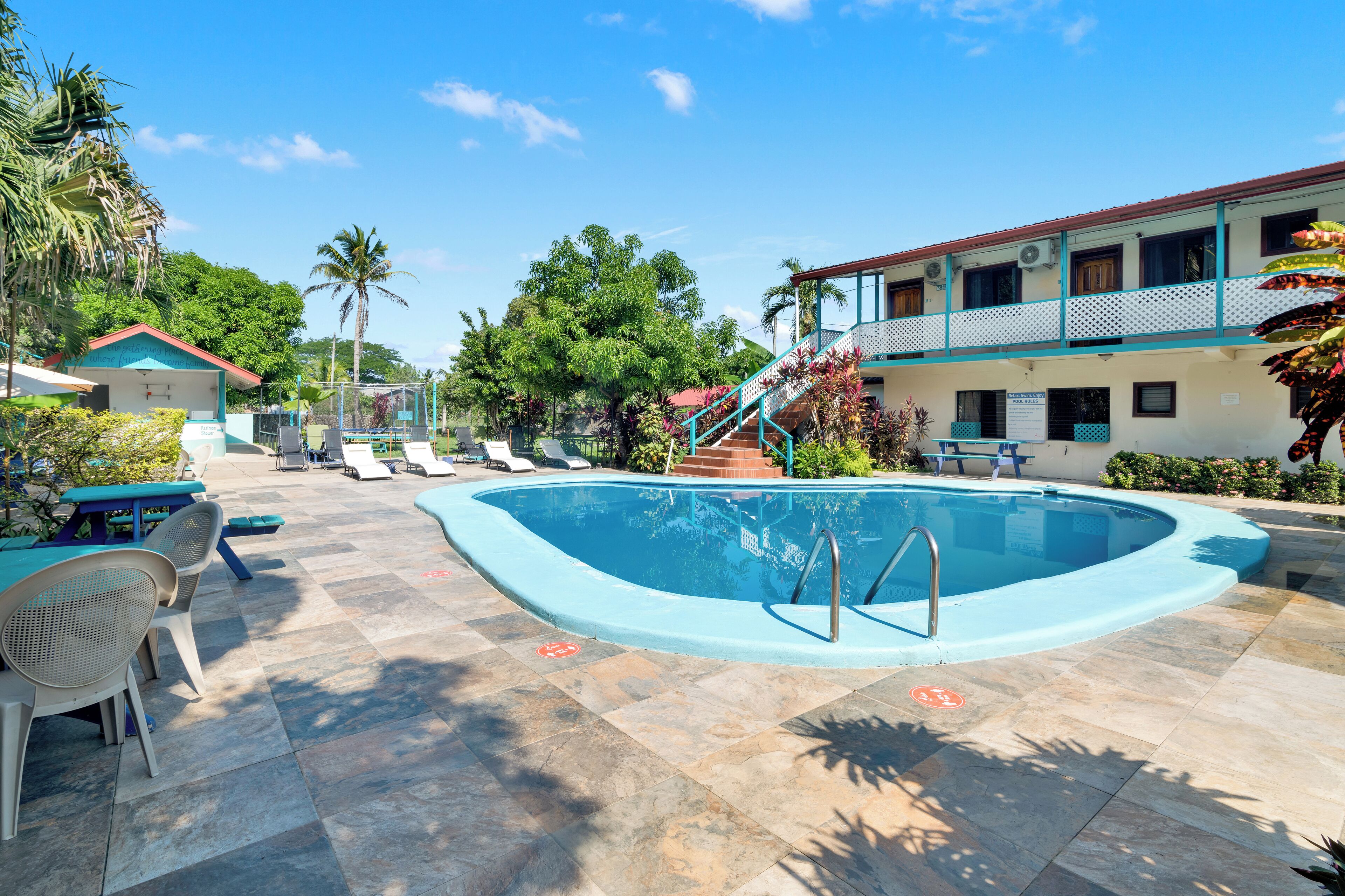 Une piscine avec des chaises longues et un escalier menant à un bâtiment doté d’un balcon.